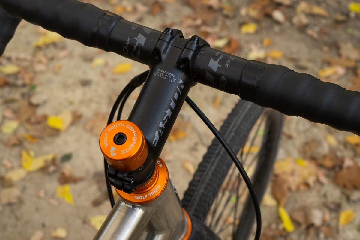 An orange Wolf Tooth Components Stem Cap sits atop an orange headset.