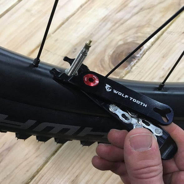 Wolf Tooth Pack Pliers, Master Link Combo Pliers, Black with Red Bolt, showed in use tightening valve stem lock nut on bicycle wheel